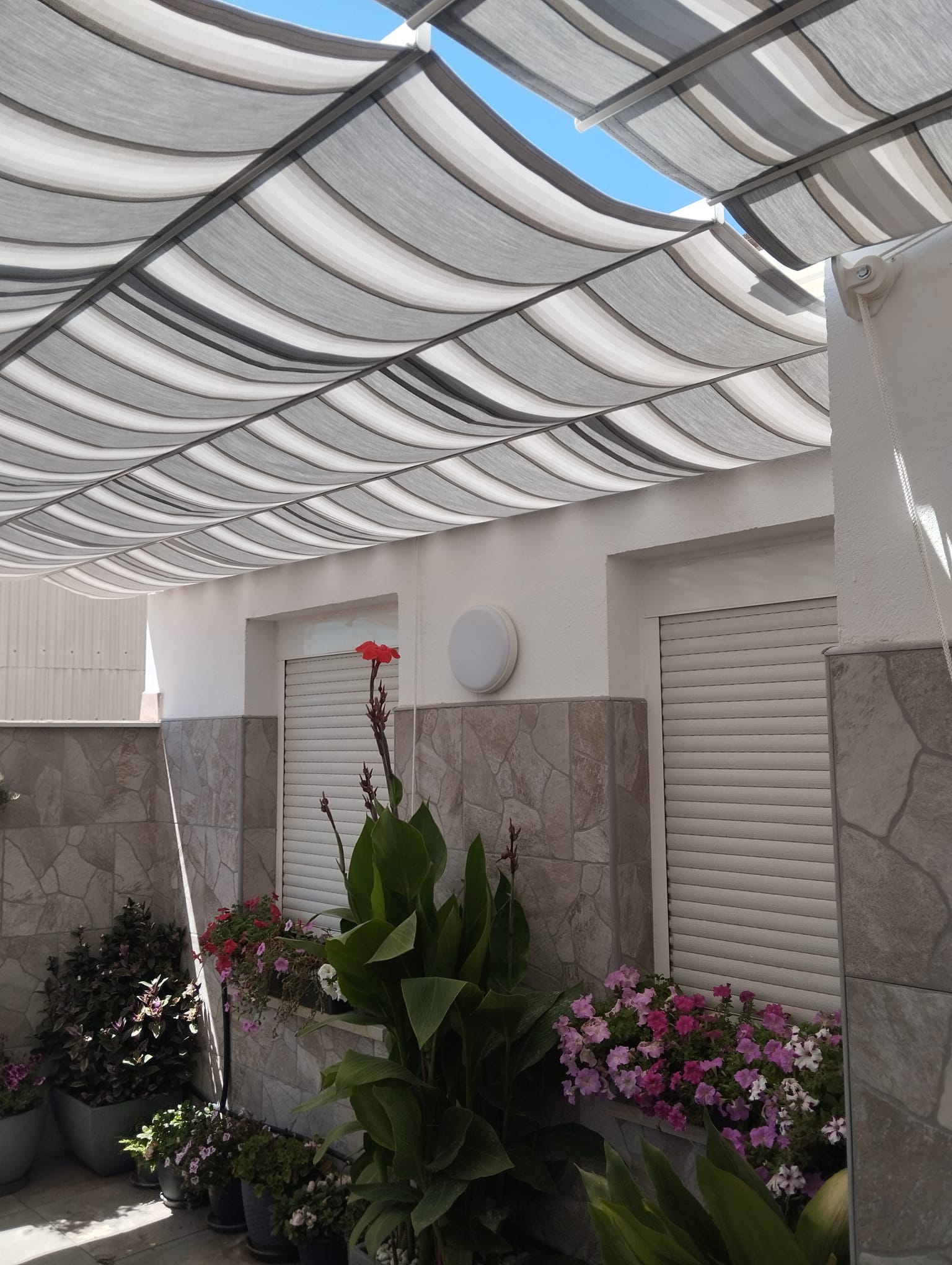 Lona de pérgola Sauleda extendida dando sombra a un patio con plantas