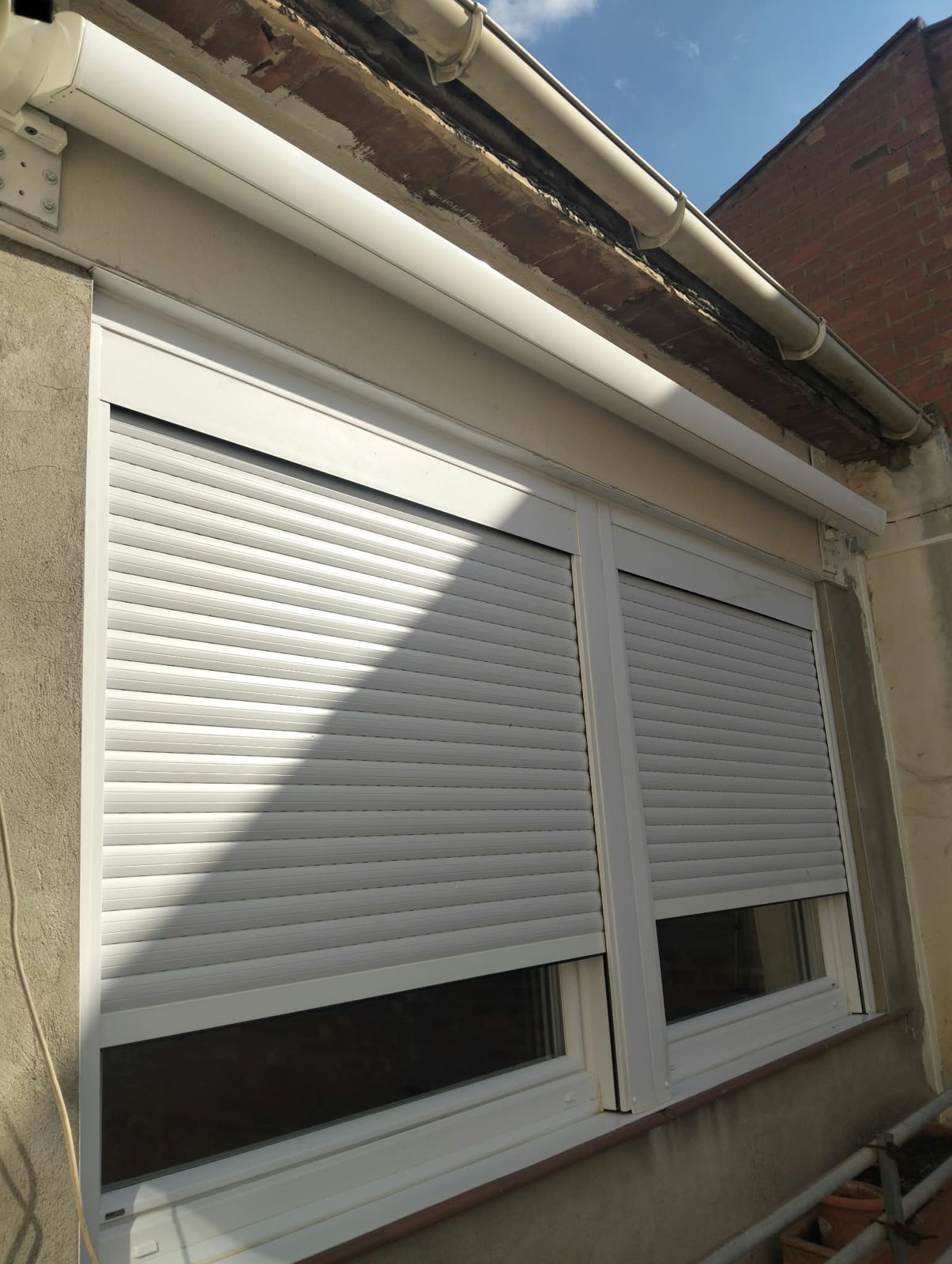 Toldo cofre blanco recogido sobre ventanas con persianas de aluminio blancas